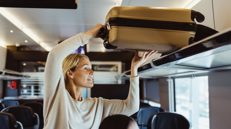 A woman lifting luggage on a train