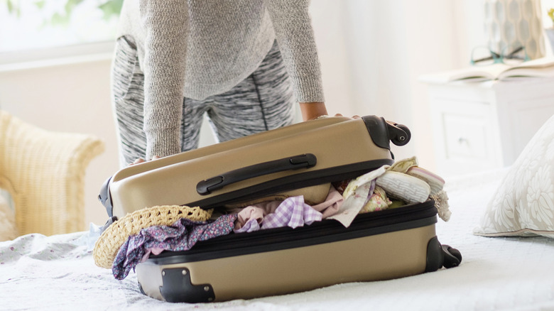 A woman tries to push closed a luggage overflowing with clothes