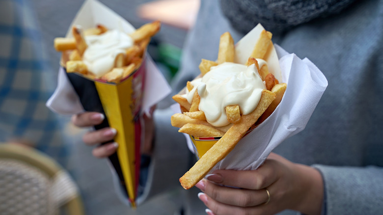 Person holding Belgian fries in a paper holder