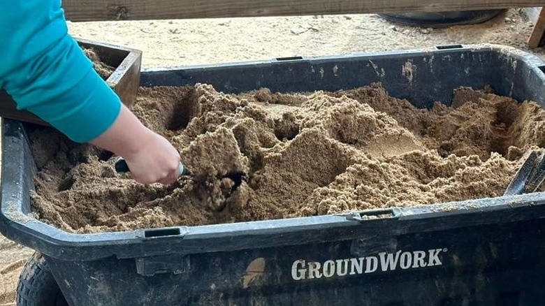 A hand sticks a shovel into a gigantic bucket of dirt at a gem mine