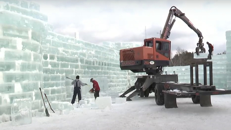 Construction vehicle and volunteers building ice palace in snow