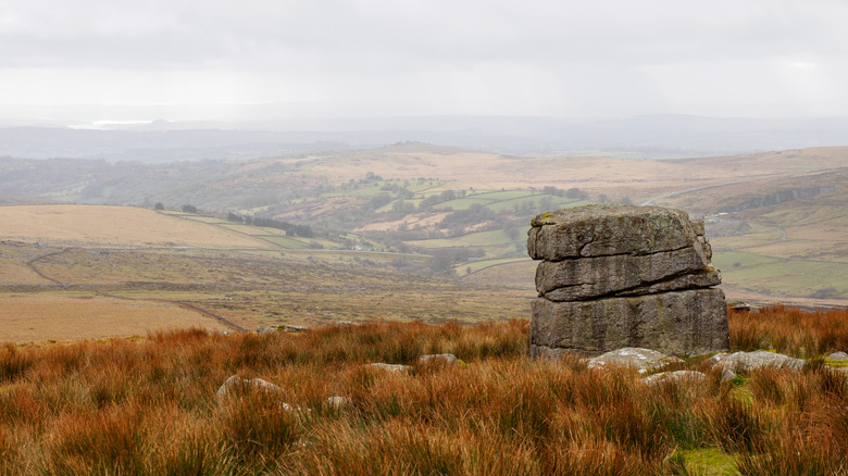 A rocky tor on a hill overlooking a misty valley in Wistman's Wood, UK