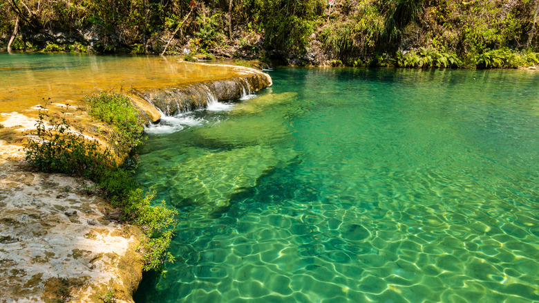 a limestone ridge and small waterfalls filling a natural turquoise pool of water