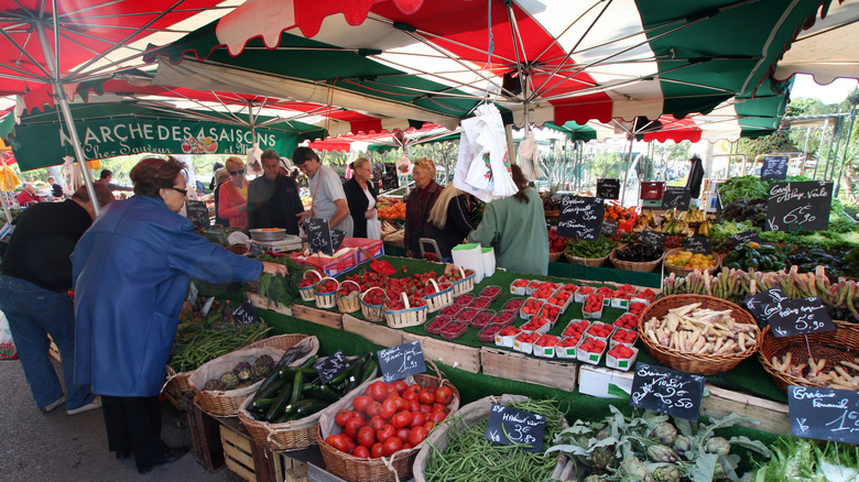 Woman in blue coat shopping at Sanary market stall with baskets of fruit and vegtable