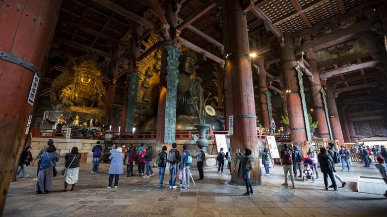 Tourists milling inside the a large wooden hall with pillars and a giant Buddha statue