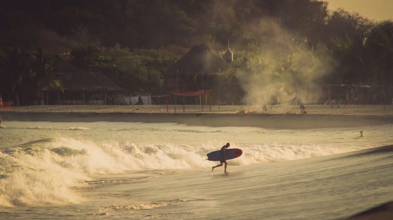 A surfer comes out of the water on the beach in Chacahua