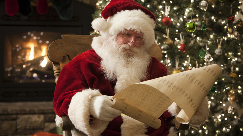 Santa reads list near a Christmas tree and fire