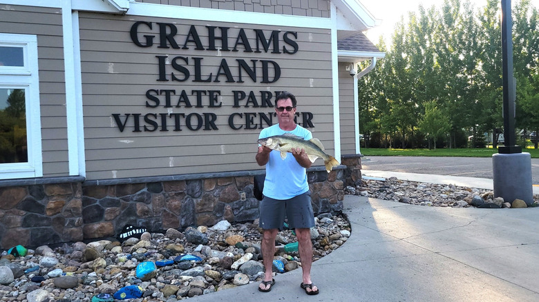 A man holding up a fish outside the Grahams Island State Park Visitor Center