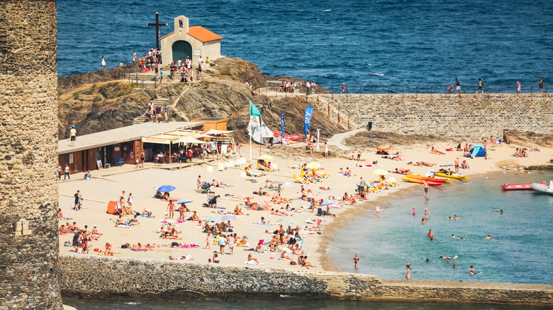 a small beach full of people surrounded by two walls with a small chapel in the background