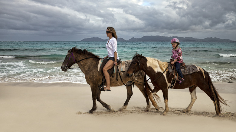 Mother and daughter ride horses on the beach