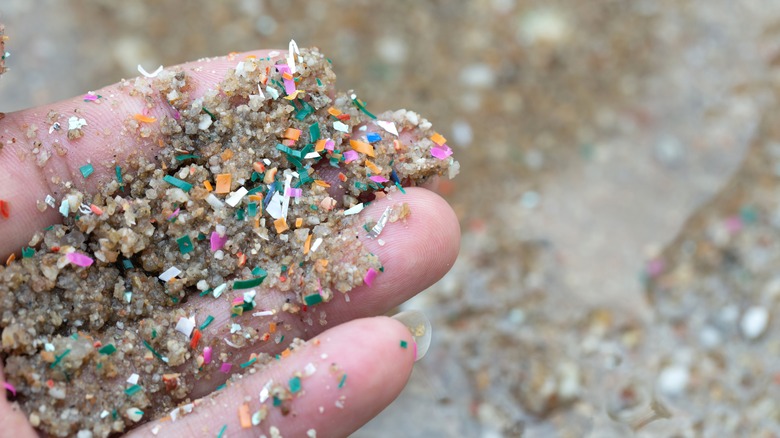 Hand holding sand with specks of broken plastic