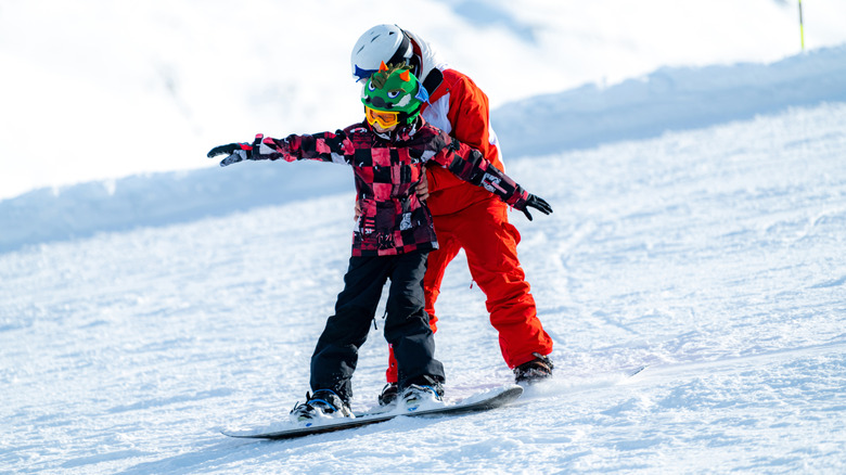 Instructor teaching a child to snowboard