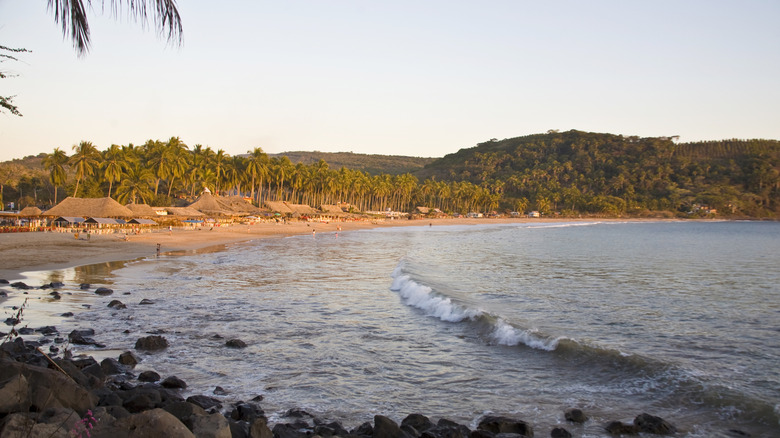 Beach and sea backed by palapas and palms in Chacala, Mexico