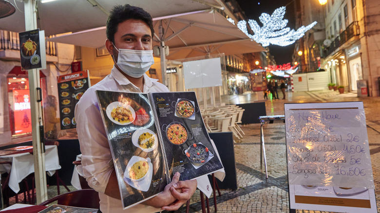 Waiter standing outside of restaurant with a menu