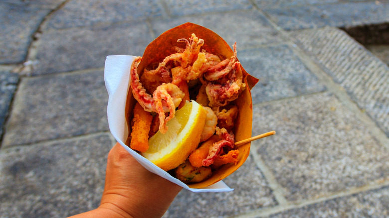 A hand holding fritto misto di pesce, a popular street food in Genoa, Italy