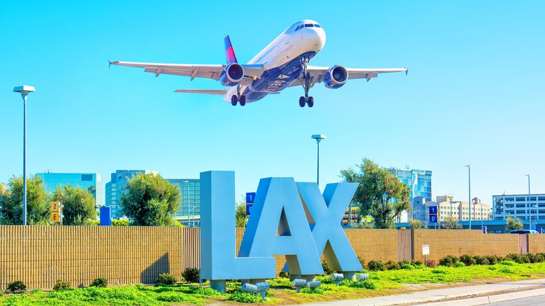 A plane flying over the LAX sign