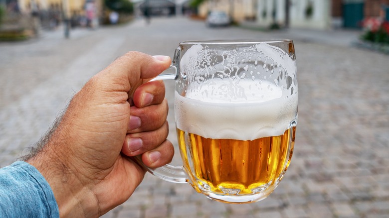 Man's hand holding beer mug in street