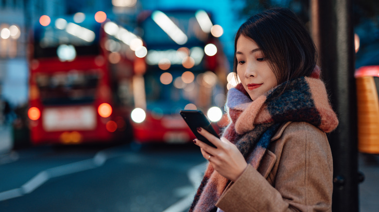 A London tourist checking her phone, buses in the background