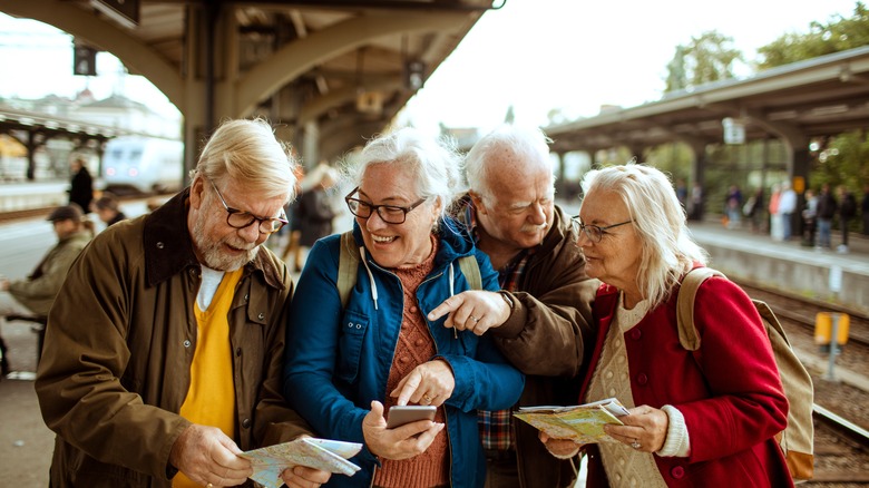 Senior travelers at a train station looking at maps and phones