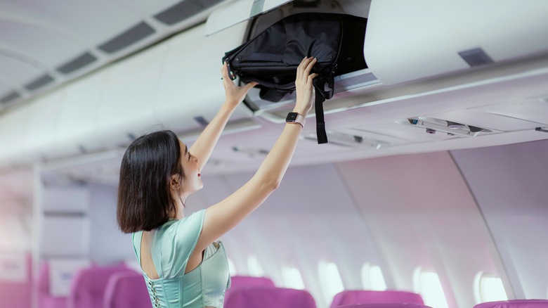 Traveler lifts bag into compartment