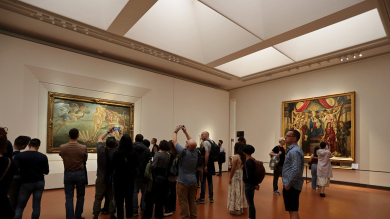 Tourists surrounding artwork hanging in Florence, Italy's Uffizi Gallery