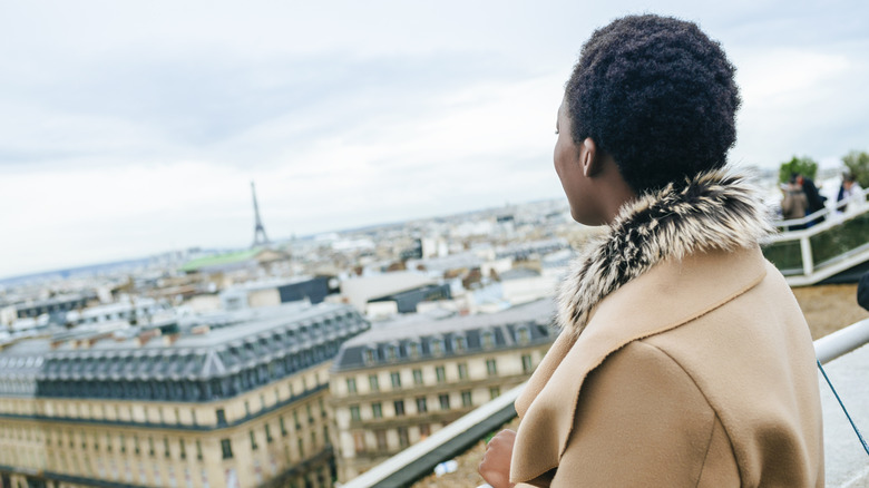 Black woman with short hair and fur collar coat looks over Paris and the Eiffel Tower