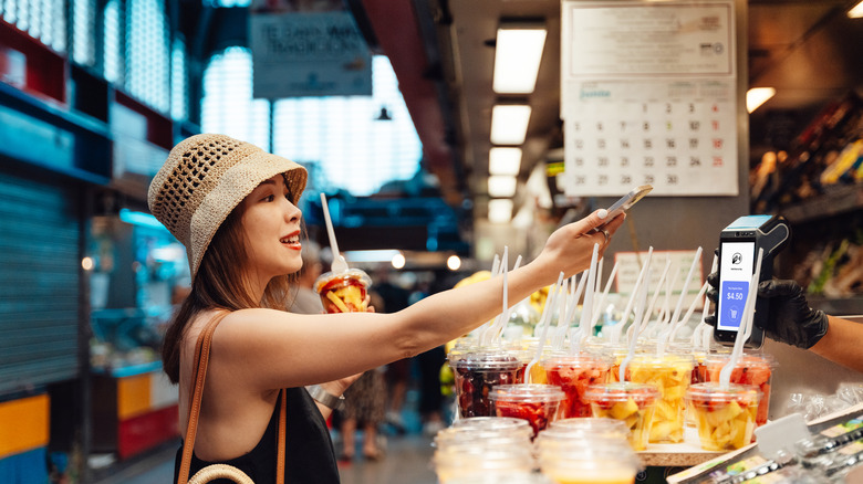 Young Asian woman with hat buying fruit at market