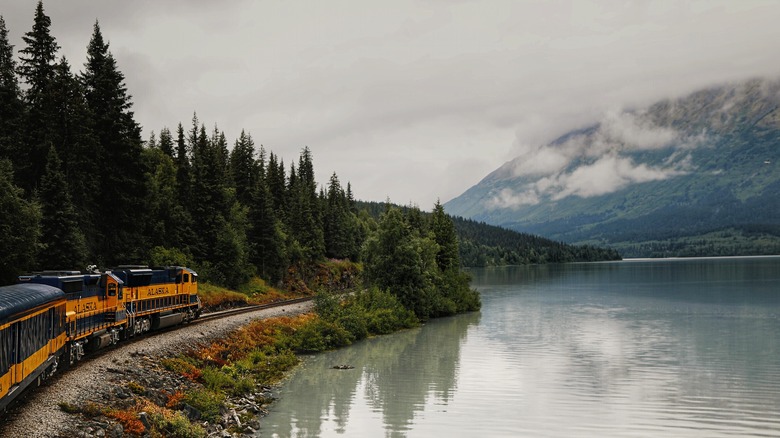 An Alaska Railroad train near a lake with mountains in the background