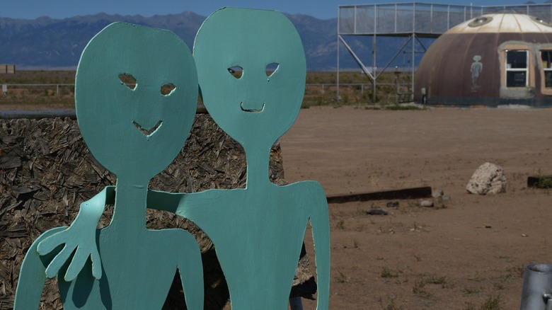 Two green alien signs in the desert in front of a dome