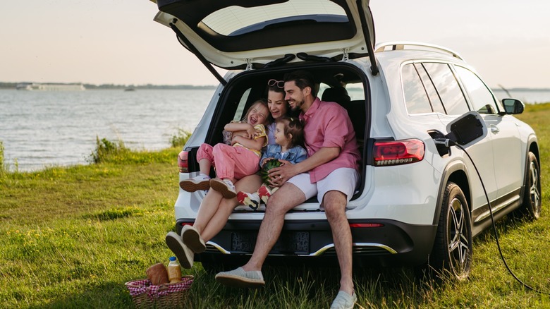 Family by a lake in the back of an EV while it charges.