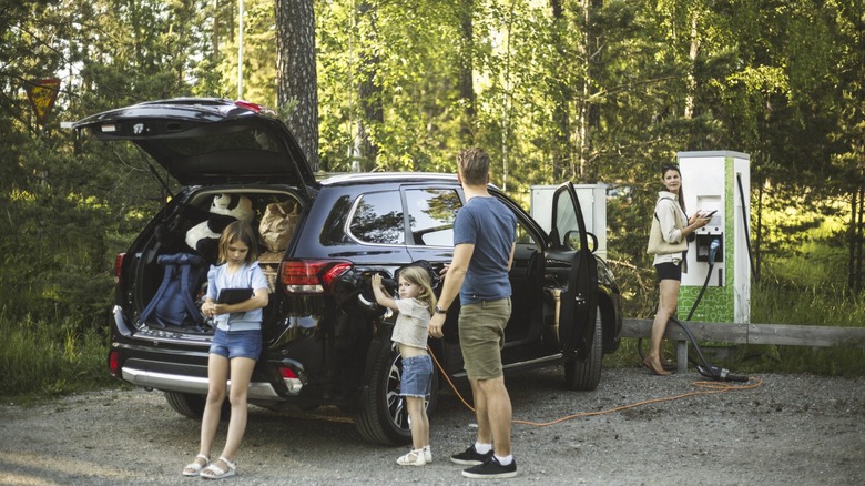 Family charging EV at charging station in the woods.