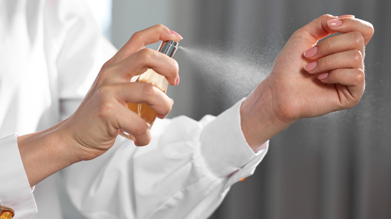 A woman sparying perfume onto a wrist.