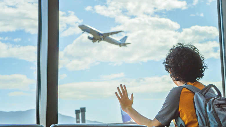 A kid staring out a window at an airplane