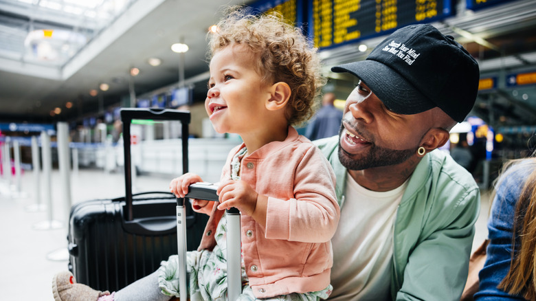 A dad and toddler girl smile at the airport