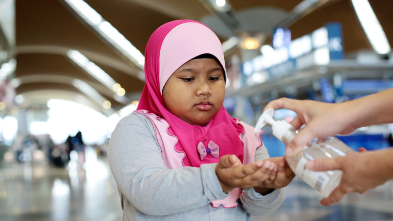 Little girl in pink hijab getting sanitizer in airport