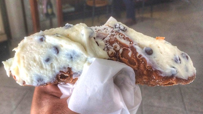 A cannolo stuffed with fresh ricotta in someone's hand