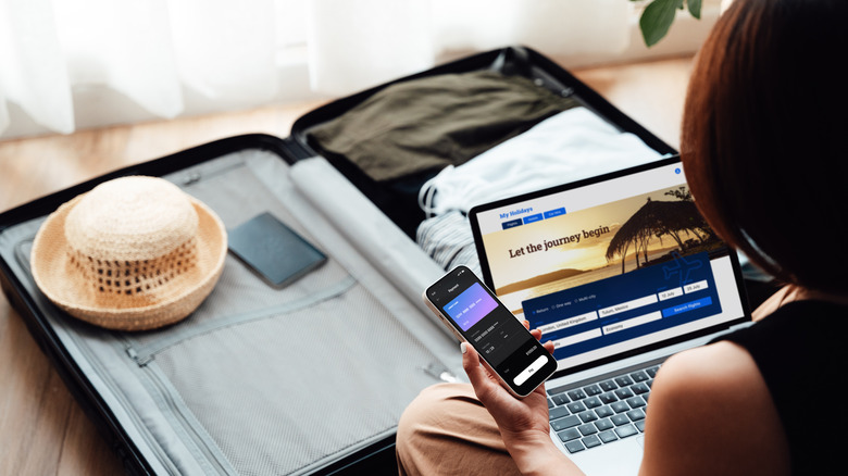 Woman booking travel on a laptop with an open suitcase