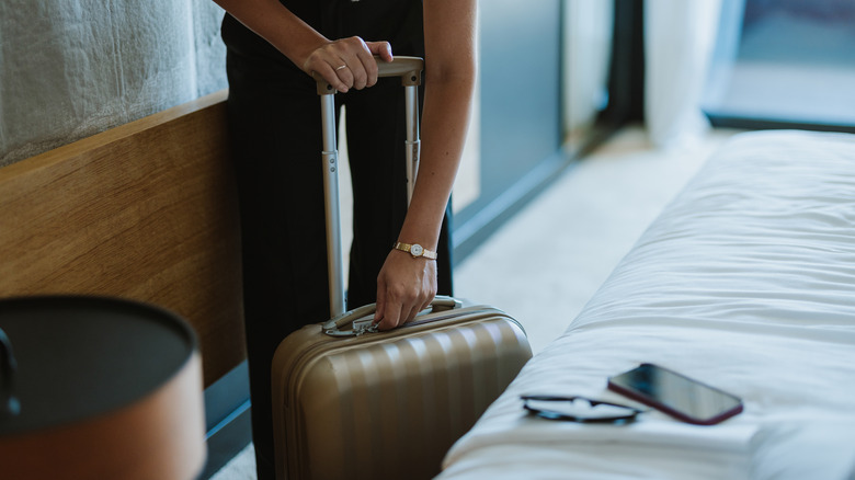 woman zipping up suitcase next to bed