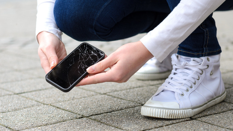 woman picking up cracked phone 