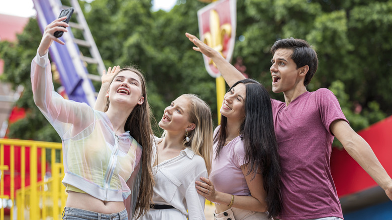 A group of friends recording footage with a smart phone at a theme park.