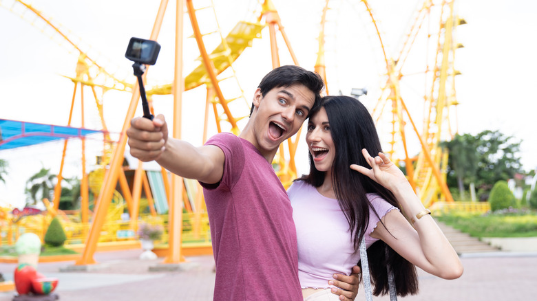 A couple posing for a photograph with a selfie stick at a theme park.