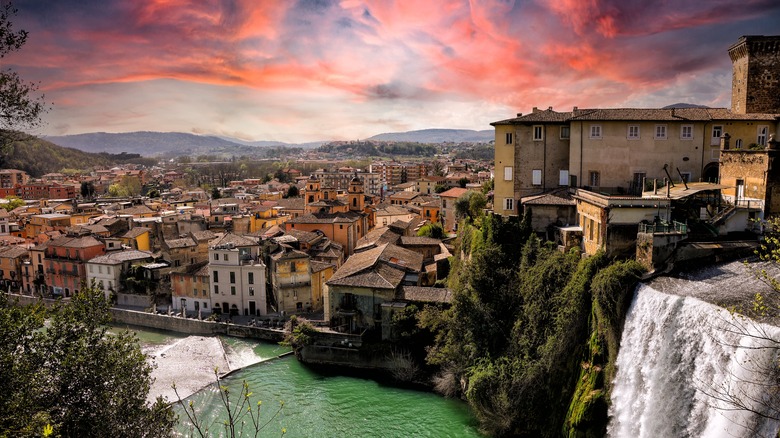 a town sits next to a river with a large waterfall as the sunset colors the sky pink