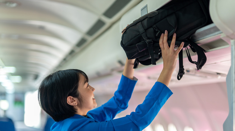 Smiling flight attendant putting bag in overhead bin