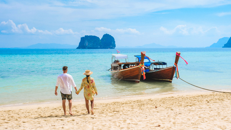 couple walking beach near boat