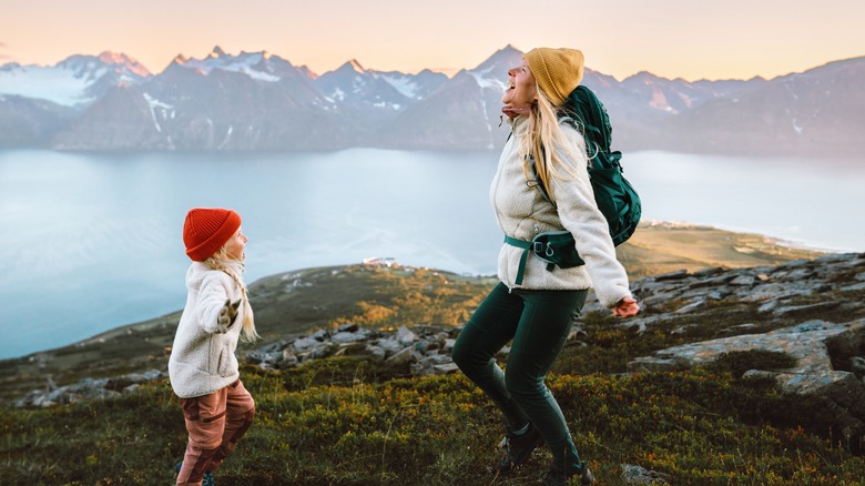 Blond woman in yellow cap dancing with child on mountaintop