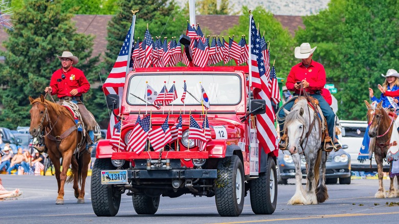 jeep covered in american flags and cowboys on horseback at cody stampede parade