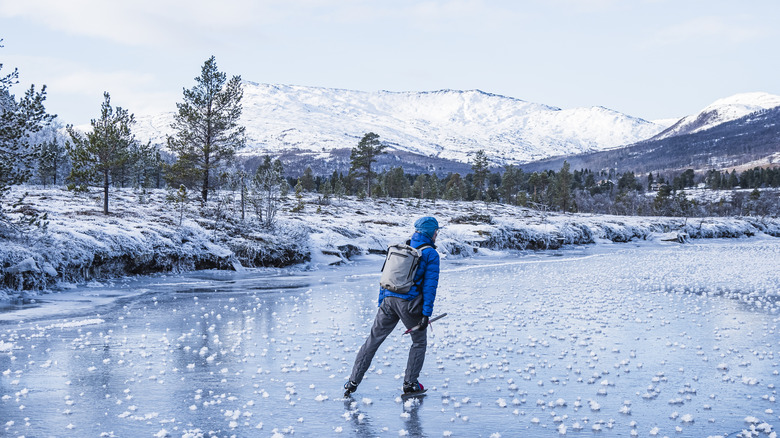 Man skating on frozen lake with mountains behind him.