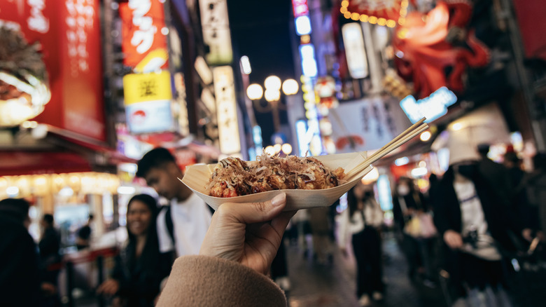 Image of woman holding a street food dish in a bustling city streets