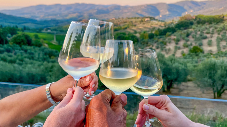 Four cheersing wine glasses overlooking vineyards