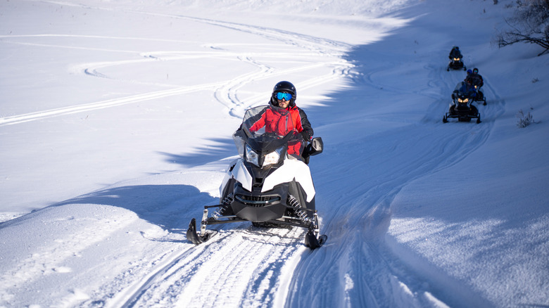 Man driving a snowmobile with three others behind him